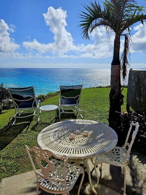 Eine Terrasse mit rundem Tisch und Stühlen, eine Palme und Blick auf den Ozean.