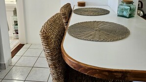 Ein Essbereich mit einem runden Tisch, gewobenen Stühlen, einem gerahmten Bild und einer kleinen Spardose.