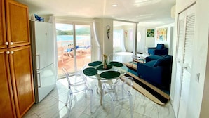 Un espacio habitable amplio con balcón, una mesa de comedor con sillas, un sofá azul y una cocina con armarios de madera y un refrigerador blanco.