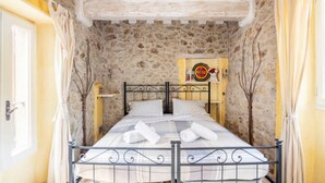 Ein Einzelbett in einem Raum mit Steinwänden, einem Metallbettgestell und einem Regal mit einer Uhr und Dekoration.