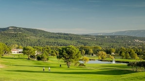 Un parcours de golf avec un étang, des arbres et des collines en arrière-plan.