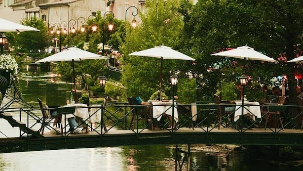 Un espace de restauration en plein air avec des tables et des chaises, des parasols et un plan d’eau en premier plan.