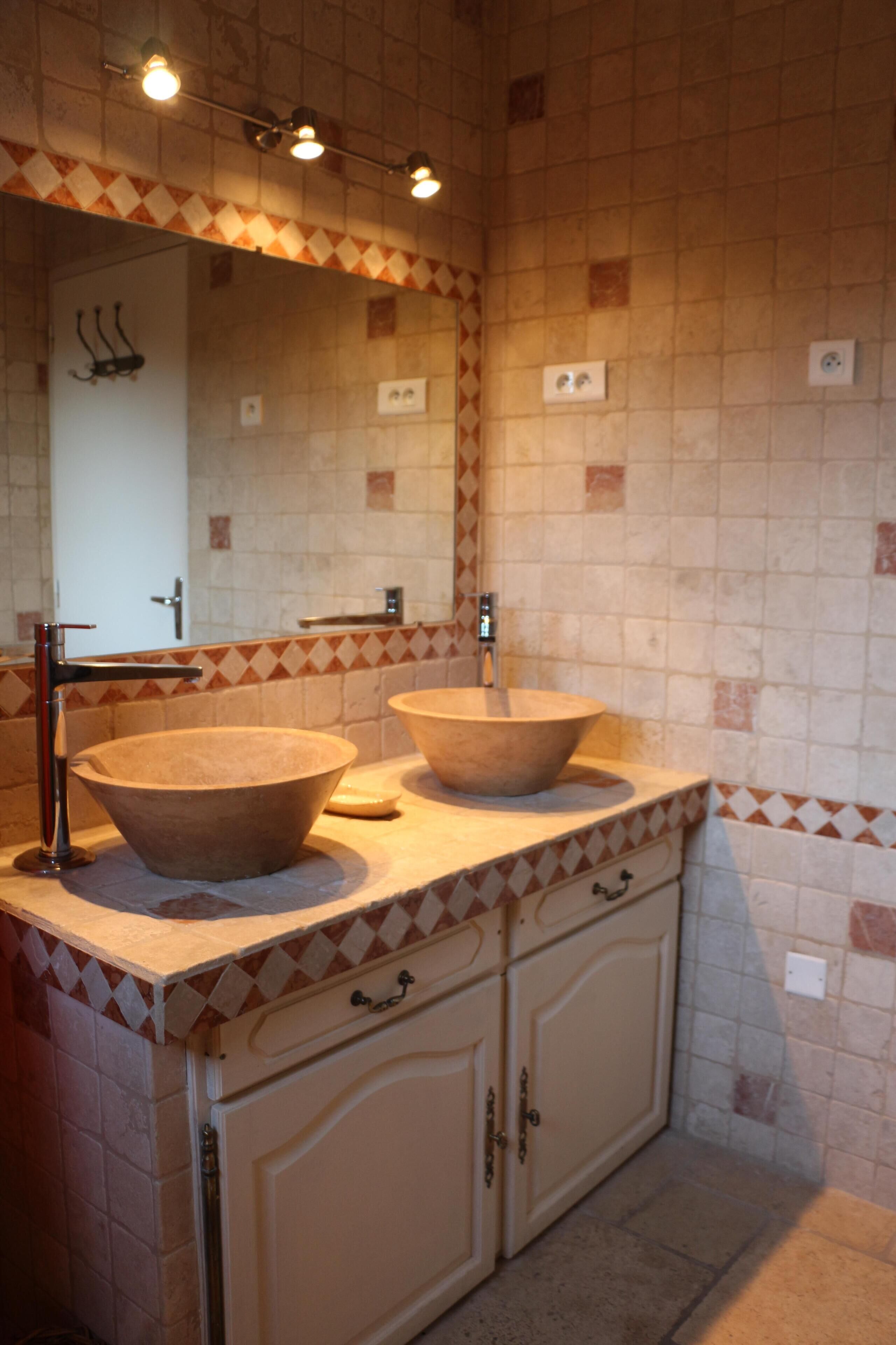 Ein Badezimmer mit zwei großen, runden Waschbecken, einem Spiegel und einer gefliesten Rückwand.