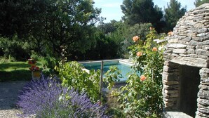 Une piscine entourée d’un jardin agrémenté de plantes de lavande et d’une structure en pierre.