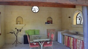 Une terrasse extérieure avec une table et des chaises en verre, un petit réfrigérateur et un comptoir carrelé avec un évier.