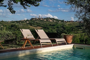 A poolside area with lounge chairs and a view of a hillside town.