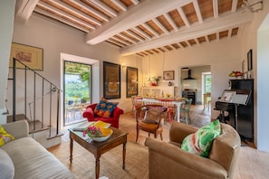A spacious living room with a dining area, a piano, and a staircase leading to a balcony.