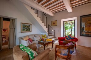 Un salon avec un escalier, un canapé, un fauteuil rouge et une table en bois.