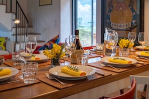 Une table à manger dressée avec des assiettes, des verres et une bouteille, avec une vue sur une fenêtre et un escalier en arrière-plan.