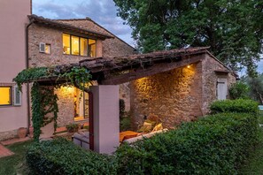 A stone house with a wooden pergola, a dog, and a chair.