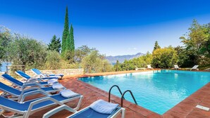 A swimming pool with lounge chairs and a stone deck, surrounded by trees and a mountain view. - Corazza 6+1, Emma Villas (Torri del Benaco)