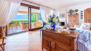 A room with a wooden cabinet, wicker furniture, a dining table with a vase of flowers, and a view of the outdoors. - Corazza 6+1, Emma Villas (Torri del Benaco)