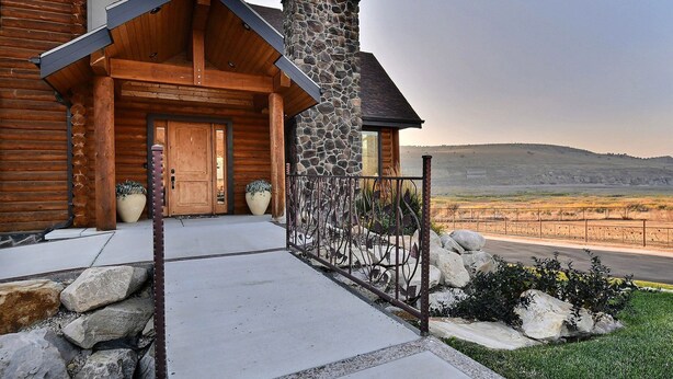 A log cabin with a stone chimney, wooden door, and a metal fence.