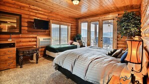 A log cabin bedroom with a bed, dresser, TV, and a balcony with a plant.