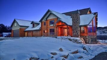 Cozy log cabin with a stone chimney and gabled roof, surrounded by a serene winter landscape.
