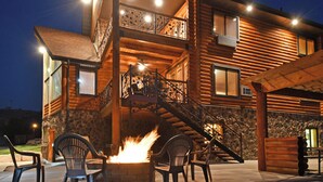 A log cabin with a stone exterior, a fire feature, outdoor seating, and a staircase leading to an upper level.