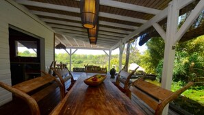 A wooden dining table with chairs, a bowl of fruit, and a hanging light fixture in a covered outdoor area with a view of greenery. - Zen Villa in residential area (Saint francois)