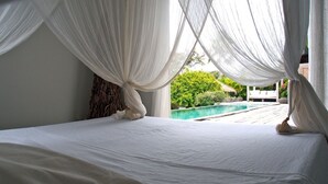 A bed with white linens and sheer white curtains, a view of a swimming pool, and greenery outside. - Zen Villa in residential area (Saint francois)