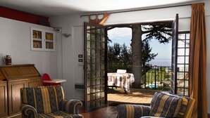 A room with patterned armchairs, a wooden table, and a view of a pool and trees through open doors. - Relax with pool and see view! (Altavilla Milicia)