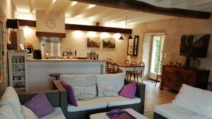 A cozy living room with a sofa set, a coffee machine, and a dining area with chairs and a table. - Beautiful stone house "country chic", private heated pool, play area (Membrey)