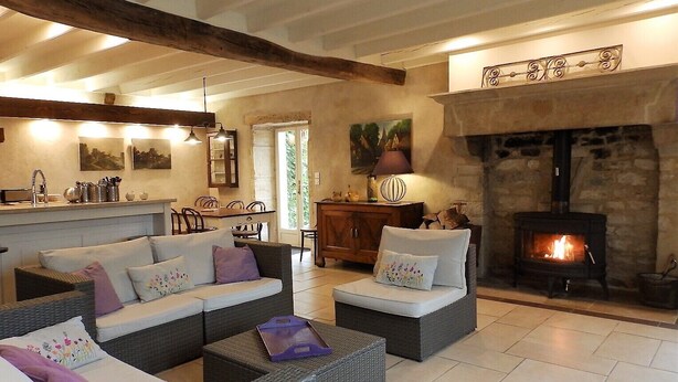 A cozy living room with a fireplace, a dining area, and a kitchen with a bar. - Beautiful stone house "country chic", private heated pool, play area (Membrey)