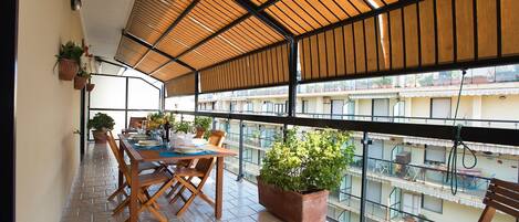 A balcony with a wooden table set for dining, potted plants, and a view of the cityscape.