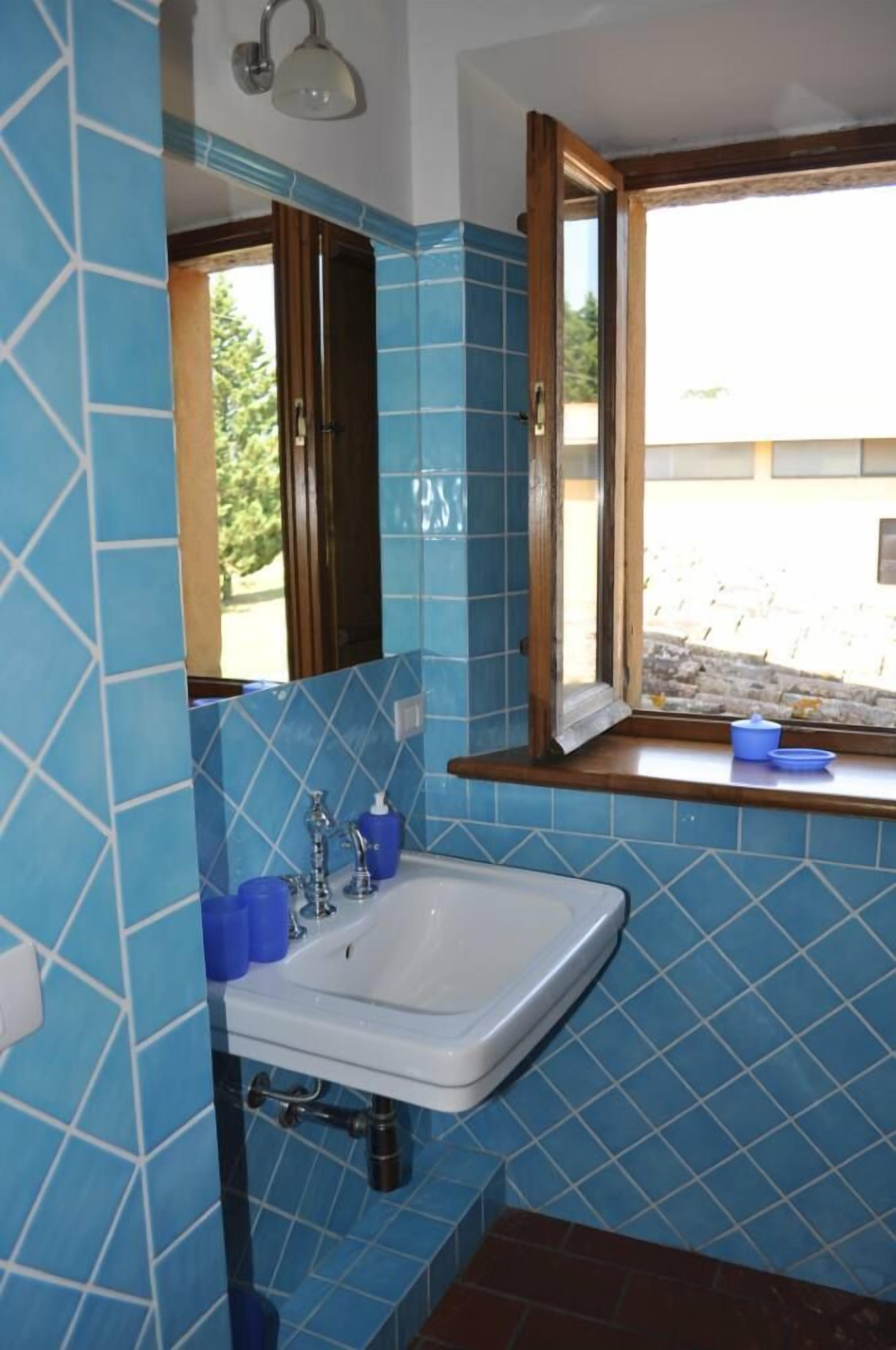 A bathroom with blue tiled walls, a white sink, and a window with a view of the outside.