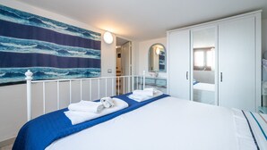 A bedroom with a bed, a dresser, a mirror, and a wall with a wave pattern. - Villa Kala Nostra by the sea, 150m and 5m walk from Kal'eMoru/Villasimius shoreline (Geremeas)