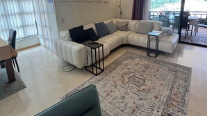 Un salon moderne avec un canapé d’angle, une petite table d’appoint, un tapis à motifs et un coin repas comprenant une table et des chaises.