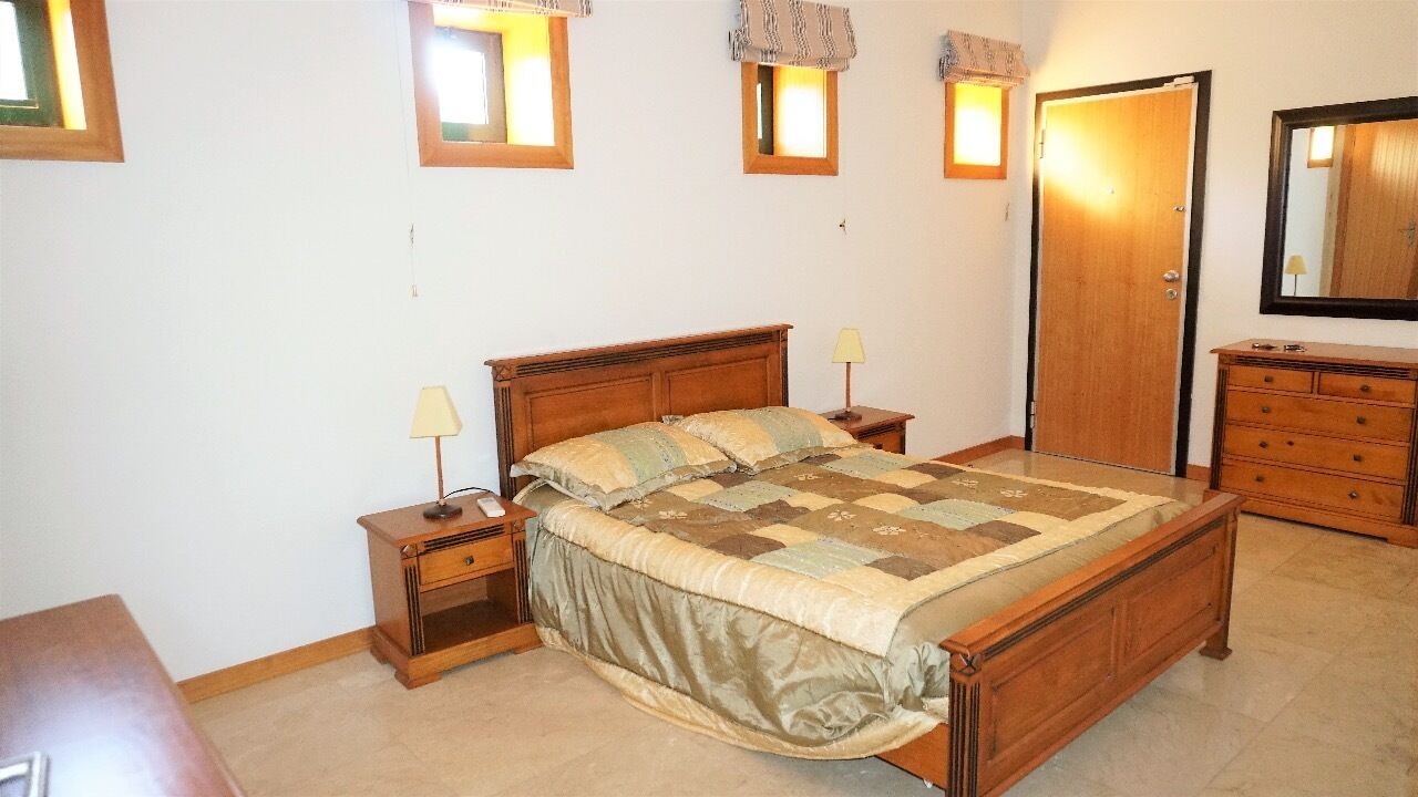 Een slaapkamer met een houten bed, twee nachtkastjes met lampen, een kaptafel en een deur.