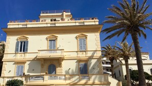 Un immeuble à plusieurs étages doté de balcons, d’une porte et de palmiers.