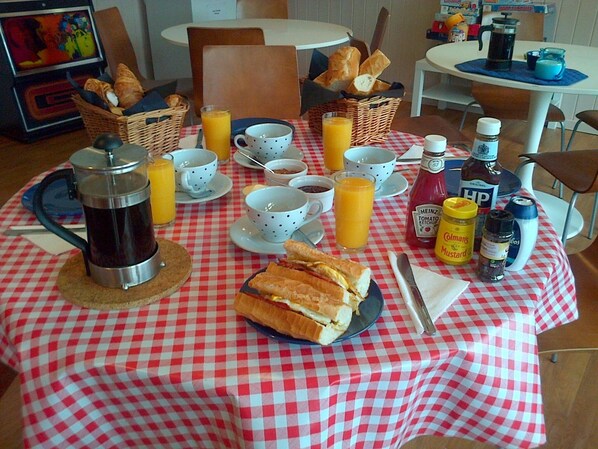 Una mesa de desayuno servida con pan, jugo, café y condimentos.
