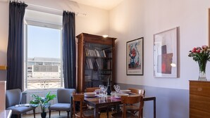 A dining area with a wooden table, chairs, a bookshelf, and a window with curtains. - Vittorio | Design and comfort in the center of Rome (Roma)