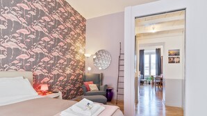 A hotel room with a bed, a nightstand, a lamp, a chair, a round mirror, and a view of the dining area. - Vittorio | Design and comfort in the center of Rome (Roma)
