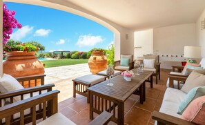 Un patio al aire libre con mobiliario de madera, una mesa y dos macetas grandes de terracota.