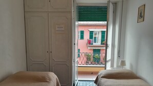 Una habitación de hotel con dos camas, una puerta cerrada y vistas a un balcón con barandilla y un edificio al fondo.