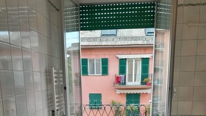 Un comedor con una mesa dispuesta para dos personas, una ventana con vistas a un edificio con balcones y un suelo de baldosas.