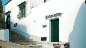 A white building with a green door and window, stone steps leading to the entrance, and potted plants on the ground. - Mariuccia House Amalfi (Amalfi)