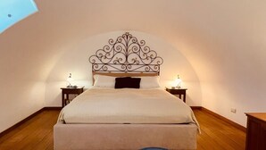 A bedroom with a curved ceiling, a bed with a decorative headboard, two bedside tables with lamps, and a wooden floor. - Mariuccia House Amalfi (Amalfi)