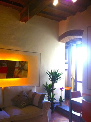 A living room with a sofa, a table, and chairs. There is a plant and a painting on the wall.