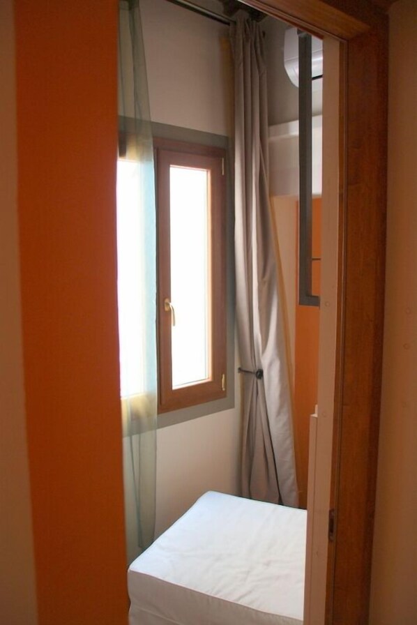 A small room with a single bed, a window with curtains, and a wooden door.