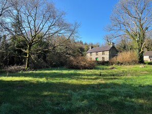 A stone house with a green door, surrounded by trees and grass.