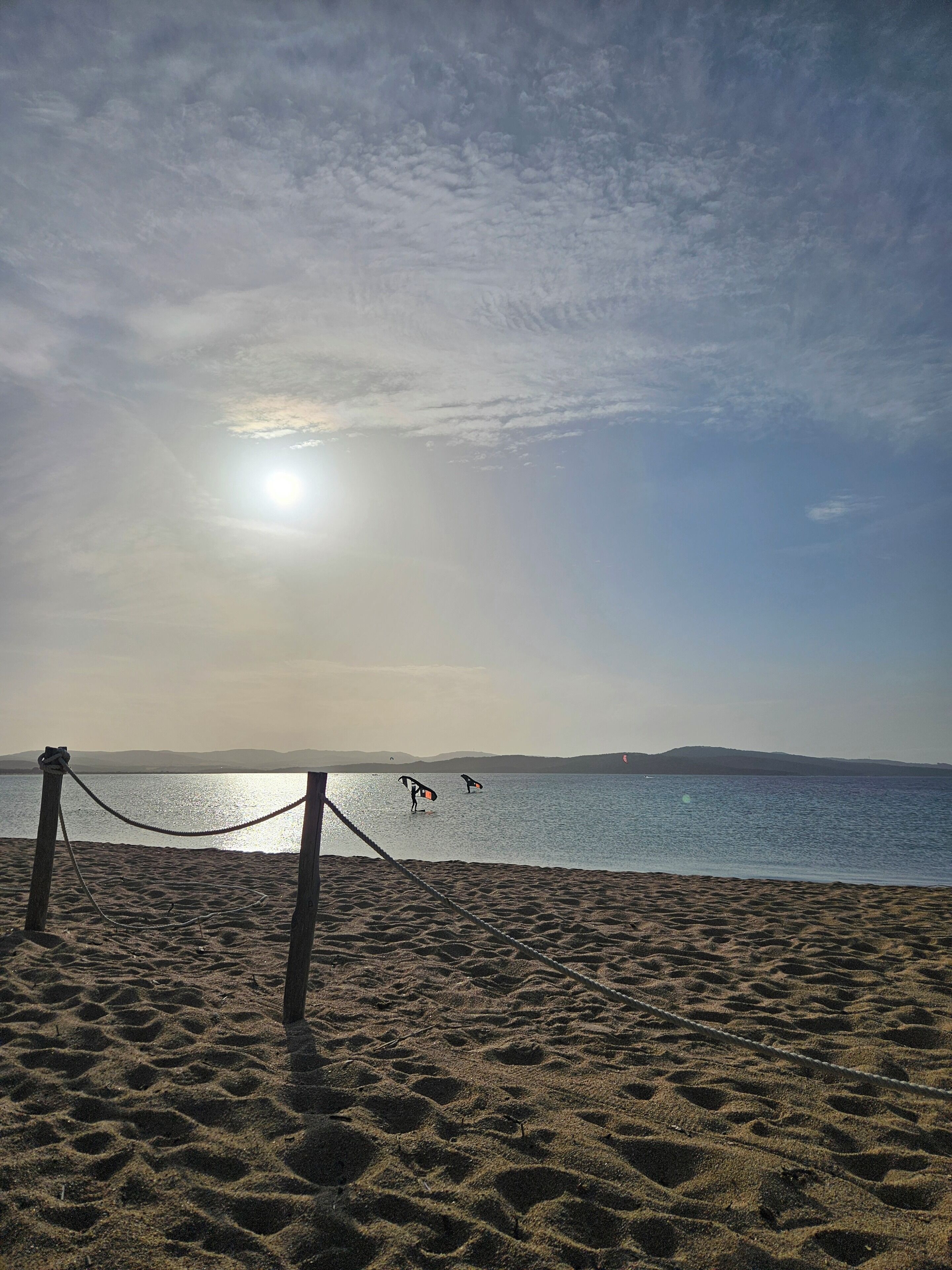 Ein Strand mit einem Seilzaun, ruhigem Wasser und Bergen im Hintergrund.