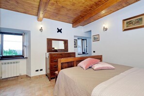 A bedroom with a wooden ceiling, a bed with pink pillows, a dresser, a mirror, and a window with a view.