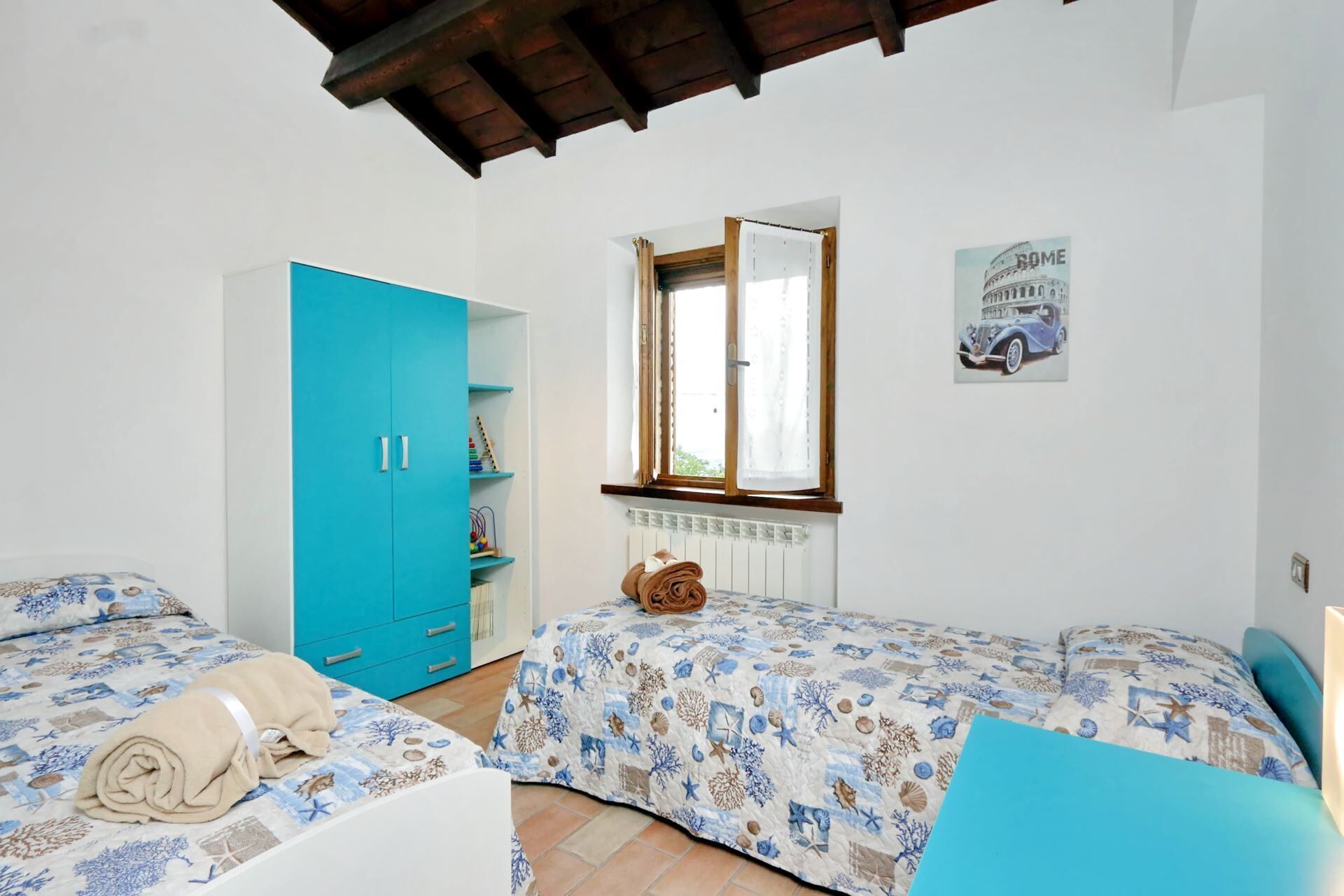 A bedroom with two beds, a blue wardrobe, a window with a view of Rome, and a radiator.