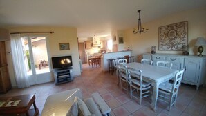 Ein geräumiger Wohnbereich mit Fernseher, Esstisch und Stühlen, eine Küche mit Schränken und einer Deckenleuchte.