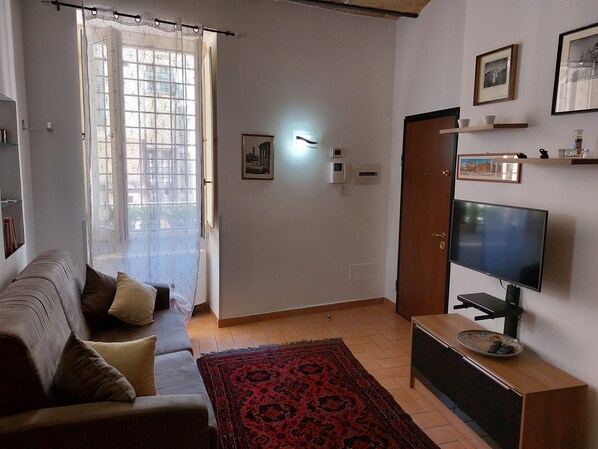 A living room with a sofa, a TV, and a patterned rug. - Elegant apartment immersed in the Fori Imperiali (Roma)