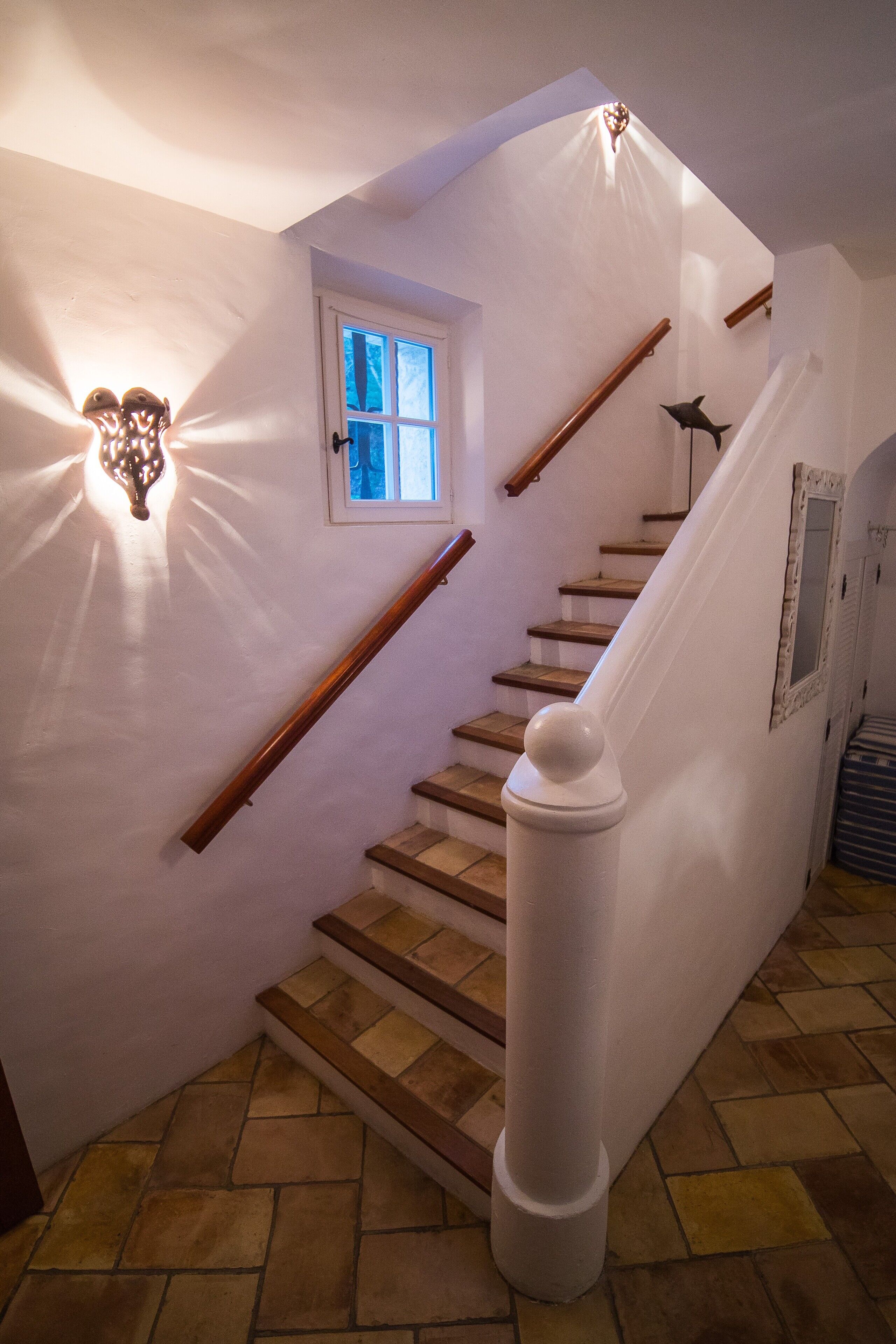 Eine Treppe mit Holzboden und weißen Geländern, die zu einer Zwischenebene mit einem kleinen Fenster führt.