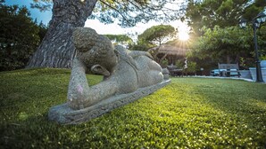 En stenskulptur af en hvilende figur i en græsplæne med træer og en lygtepæl i baggrunden.