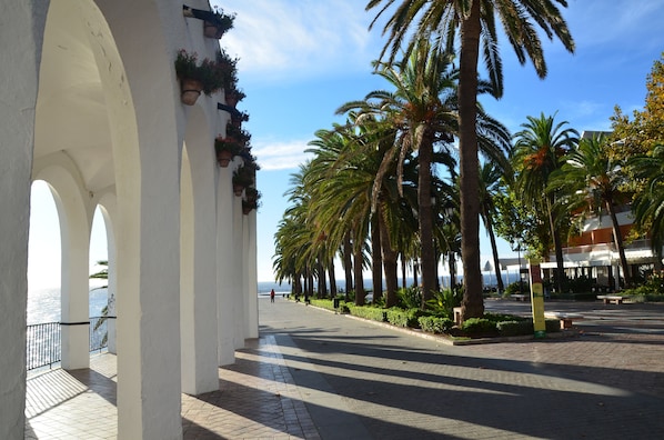 A coastal promenade with white arches, palm trees, and a view of the sea.